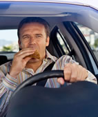 Beim Autofahren sollte sich der Fahrer auf den Verkehr konzentrieren und nicht essen oder auf dem Handy tippen. Sonst steigt die Unfallgefahr deutlich